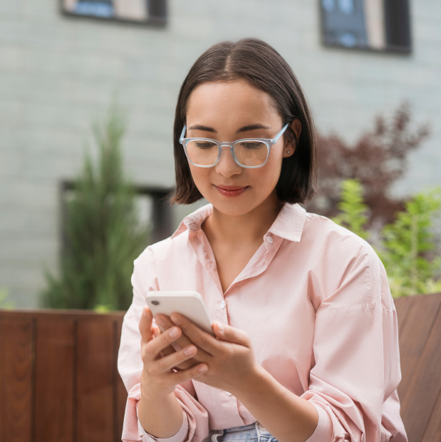 A young woman sitting outside on her phone, booking an appointment at Vitality Medical Wellness Center for facial rejuvenation in Belle Meade.